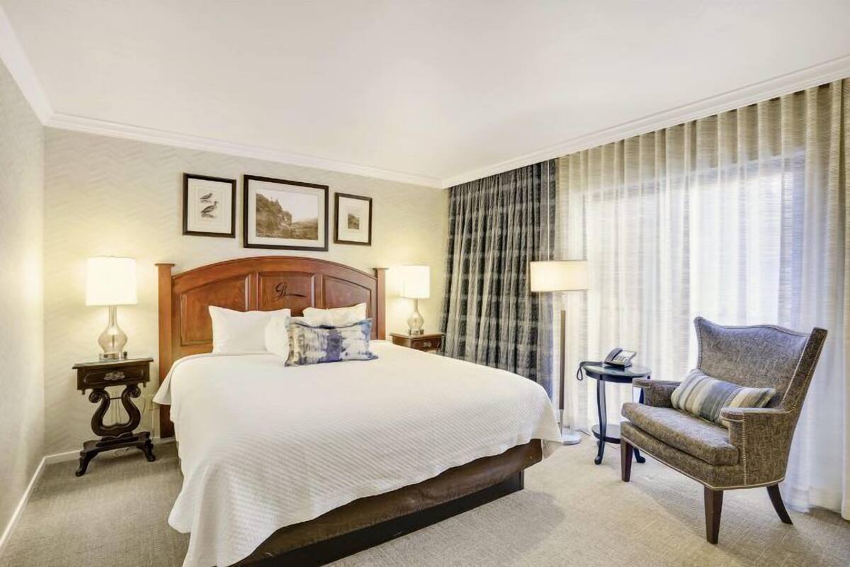 A hotel room with a large bed, two bedside tables with lamps, a chair, and a view of the outdoors.