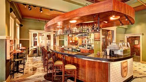 A bar area with a curved wooden counter, multiple stools, and a variety of bottles and glasses. - Hotel Boulderado (Boulder)