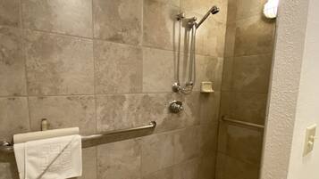 A shower area with beige tiles, a handrail, a towel, and a handheld showerhead.