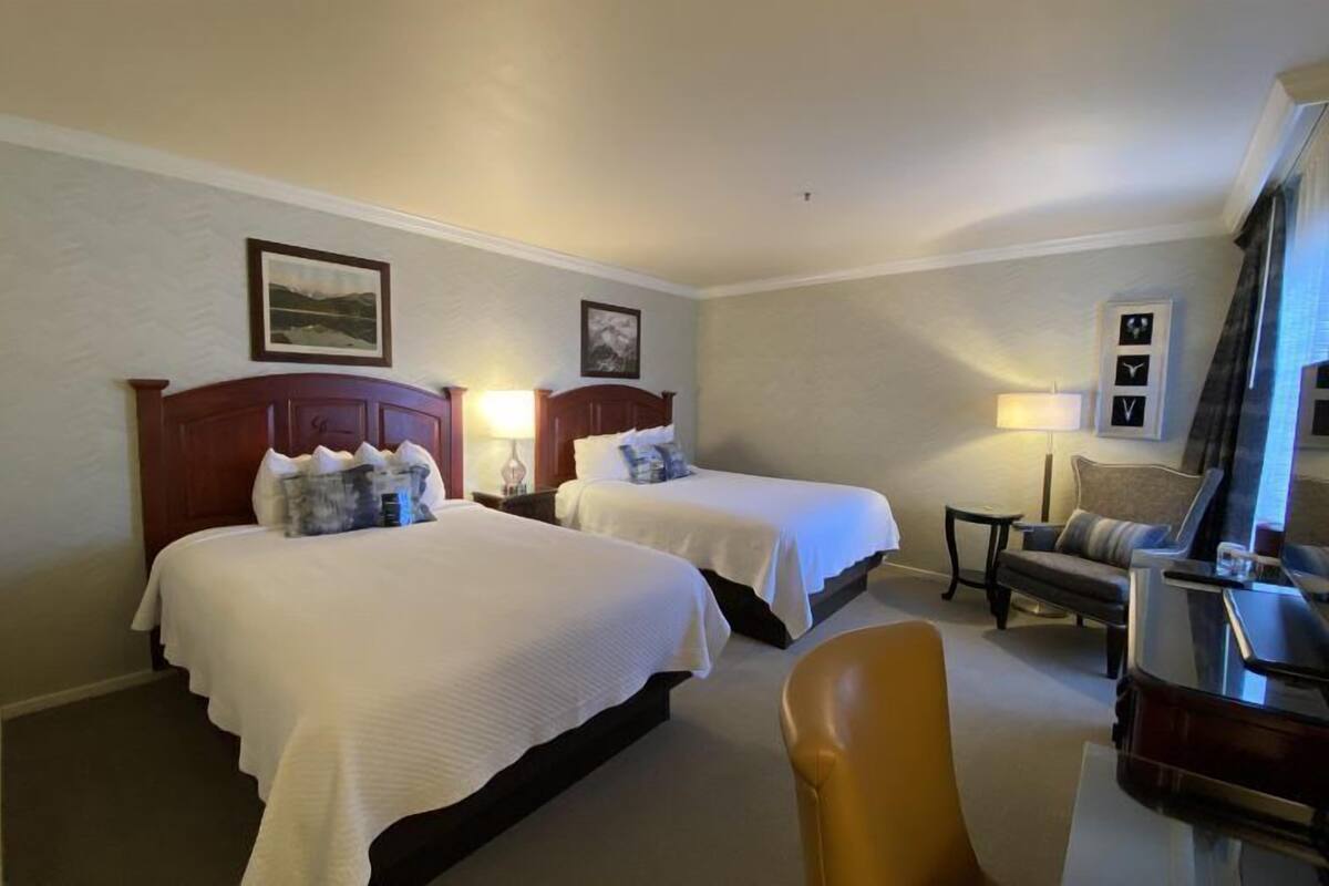 A hotel room with two beds, a desk, a chair, and a small table.