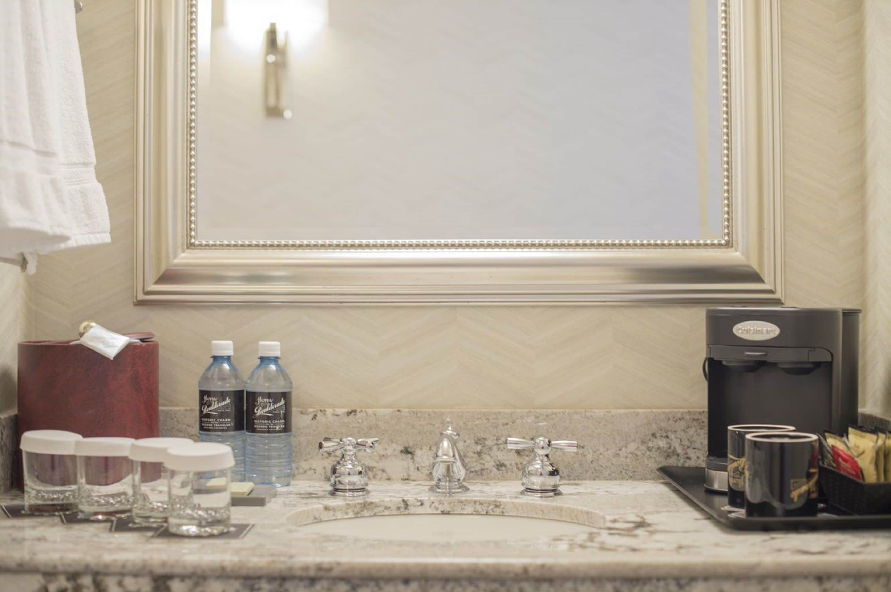 Un bagno con un grande specchio, due lavandini, una macchina per il caffè e articoli da toilette sul ripiano.