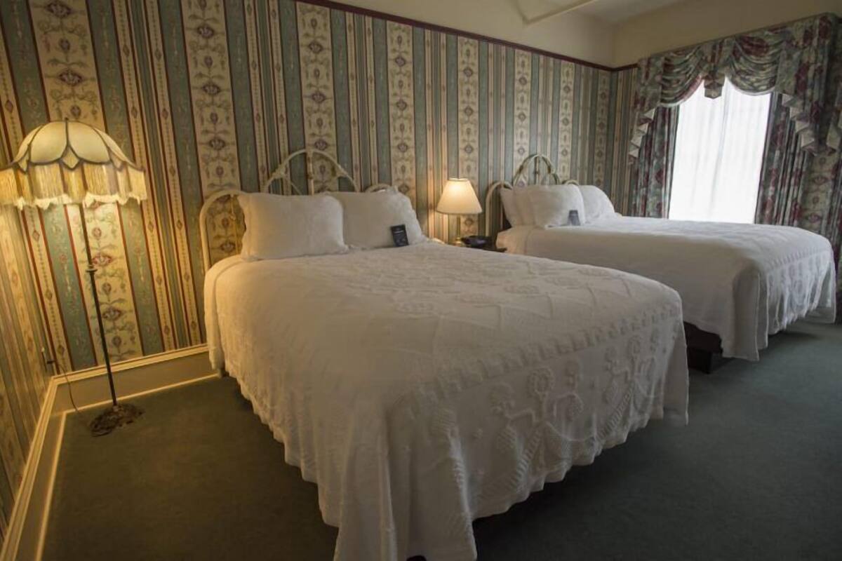 A hotel room with two beds, a patterned wallpaper, and a lamp.