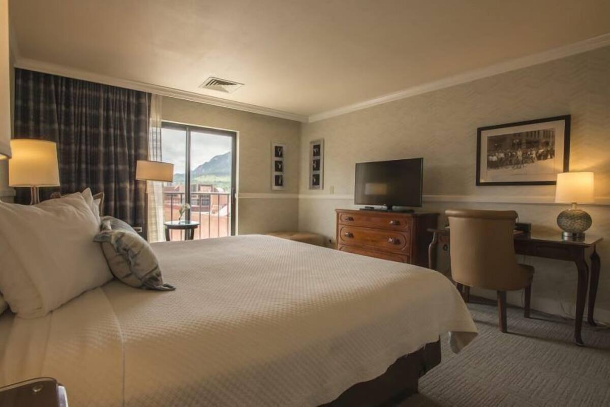 A hotel room with a large bed, a desk, a chair, a television, and a window with a view of mountains.