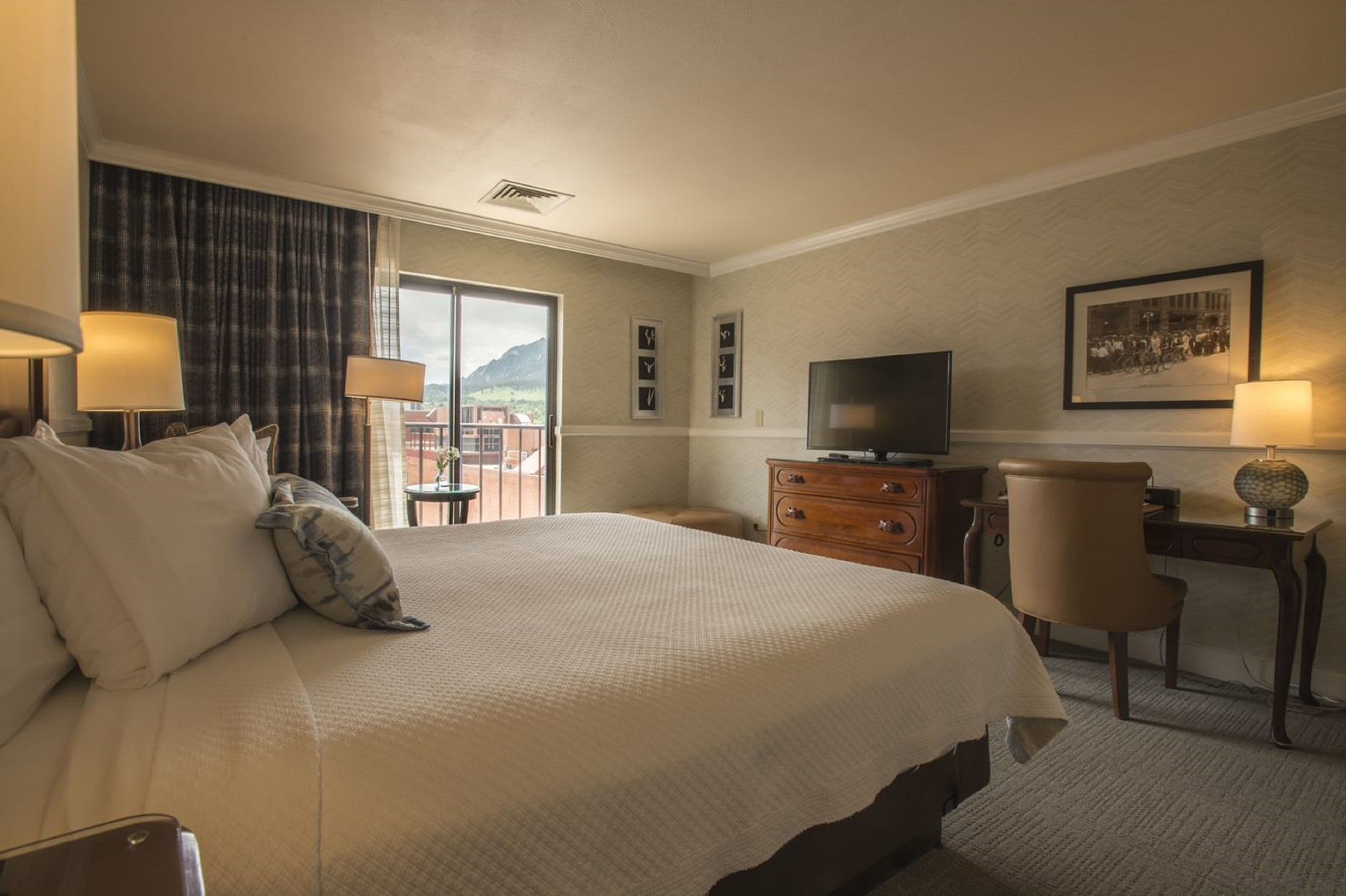 Ein Hotelzimmer mit einem großen Bett, einem Schreibtisch, einem Sessel, einem Fernseher und Blick auf Berge durch das Fenster.