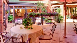 A patio area with a round table, chairs, and a red umbrella. There are potted plants and a brick building in the background. - Hotel Boulderado (Boulder)