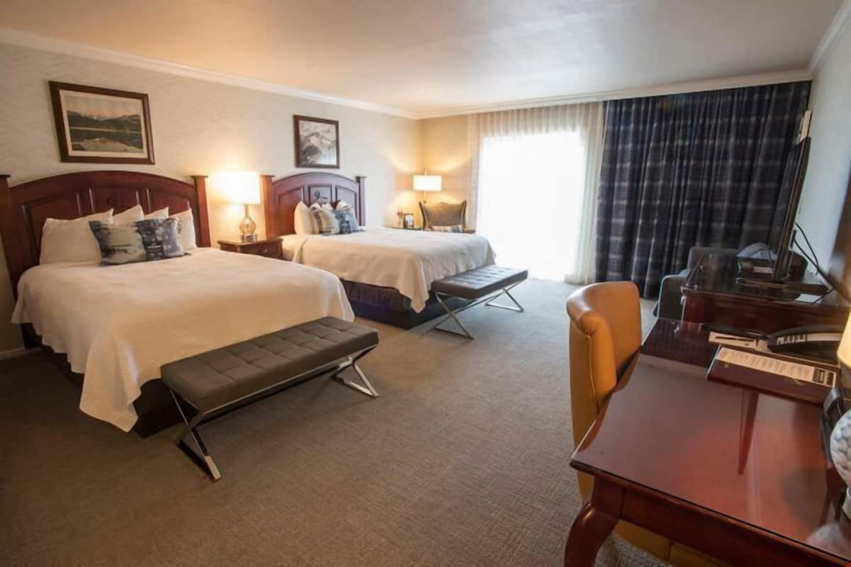 A hotel room with two beds, a desk, a chair, and a bench.