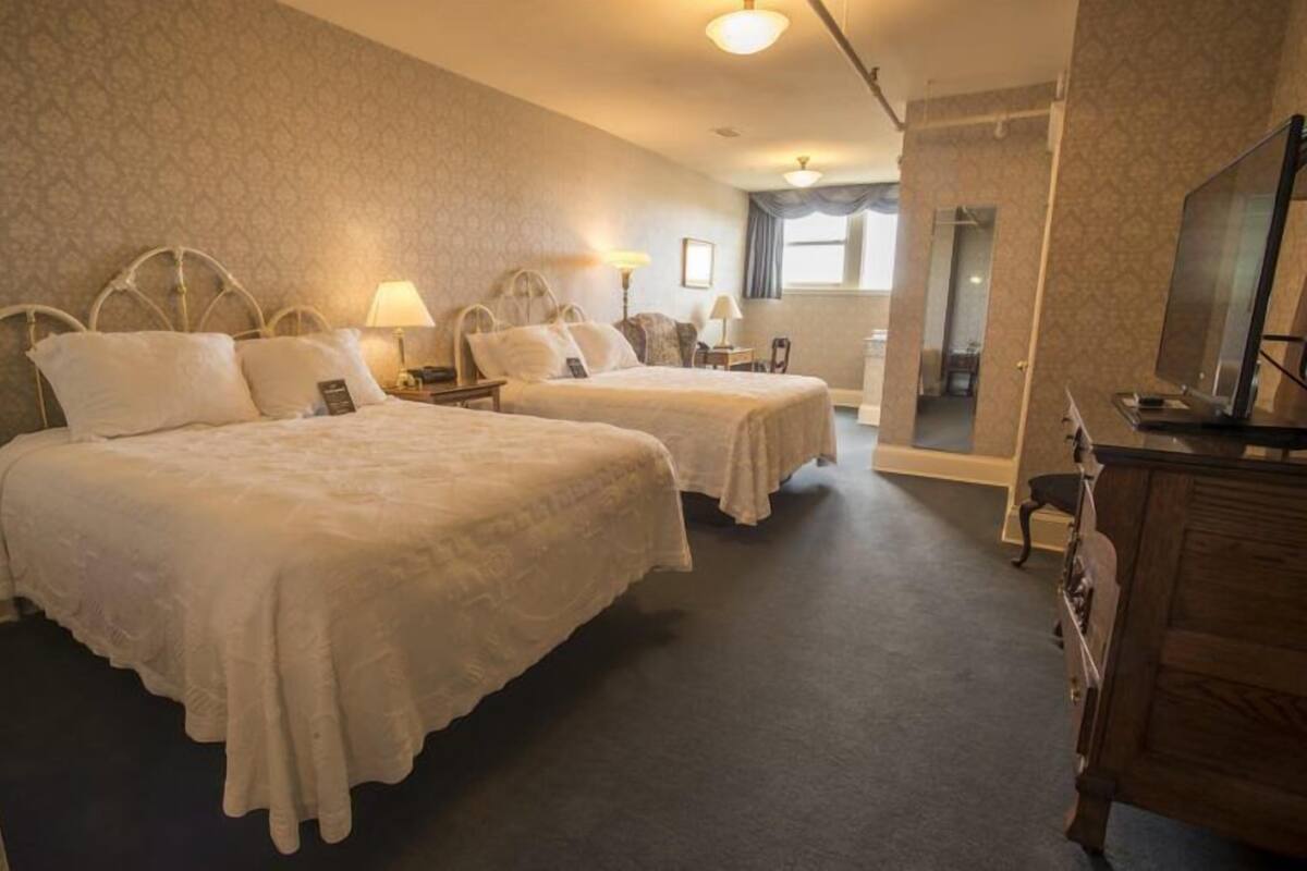 A hotel room with two beds, a dresser, a television, and a mirror.