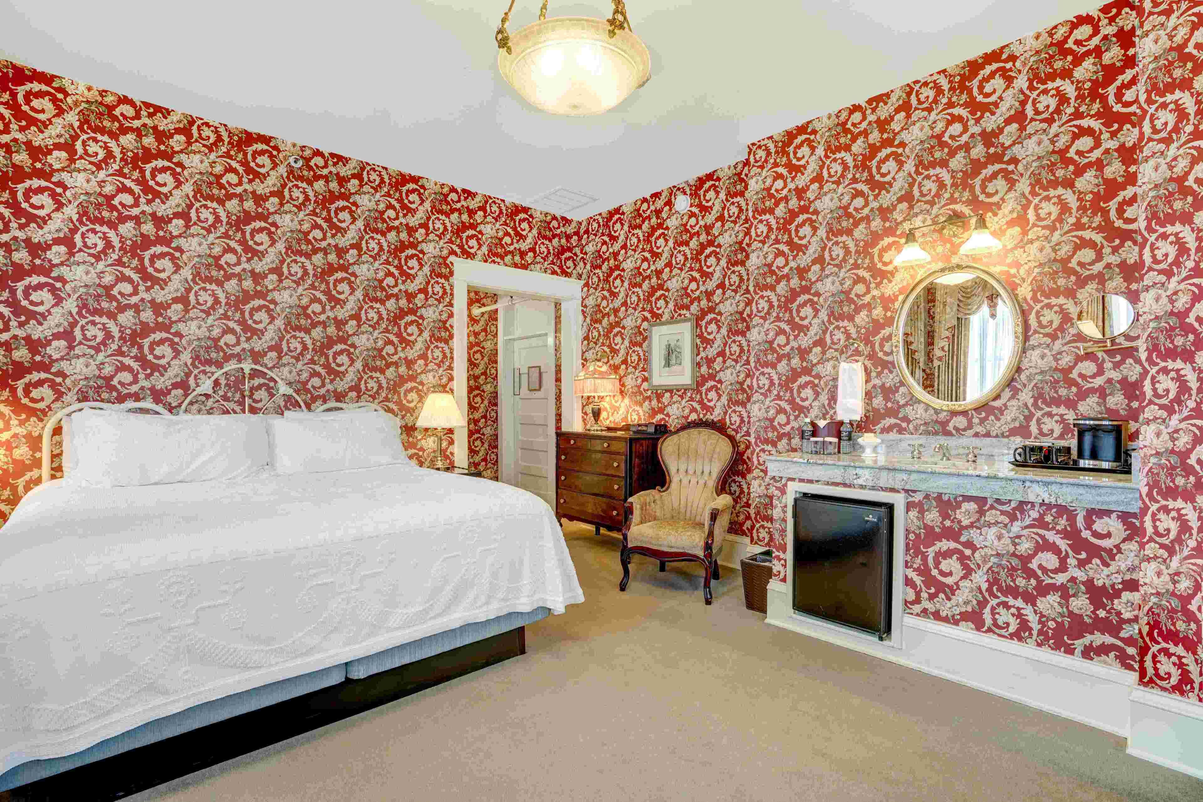 A bedroom with a large bed, a dresser, a chair, a mirror, and a fireplace.