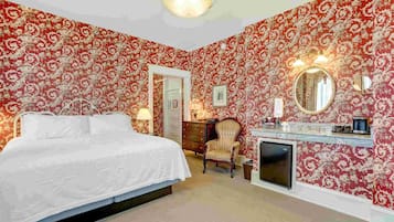 Um quarto com uma cama grande, cômoda, cadeira, espelho e lareira.
