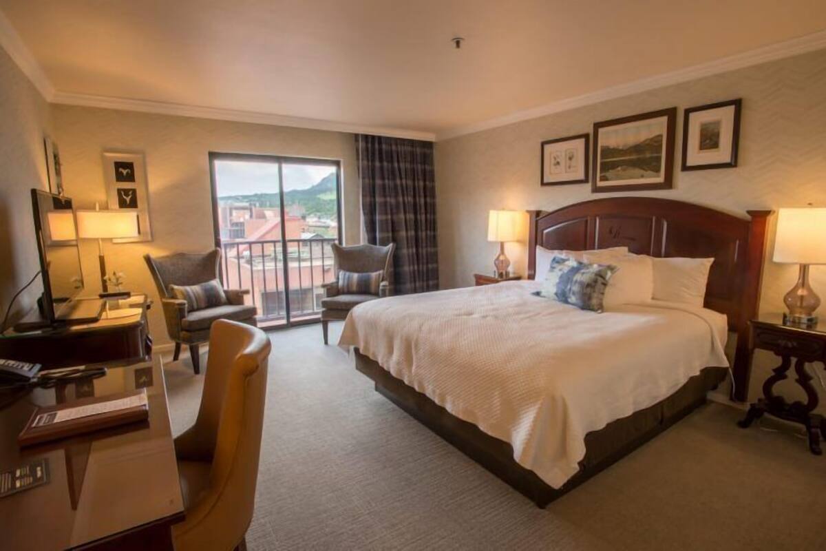 A hotel room with a bed, desk, chair, and a balcony with a view.