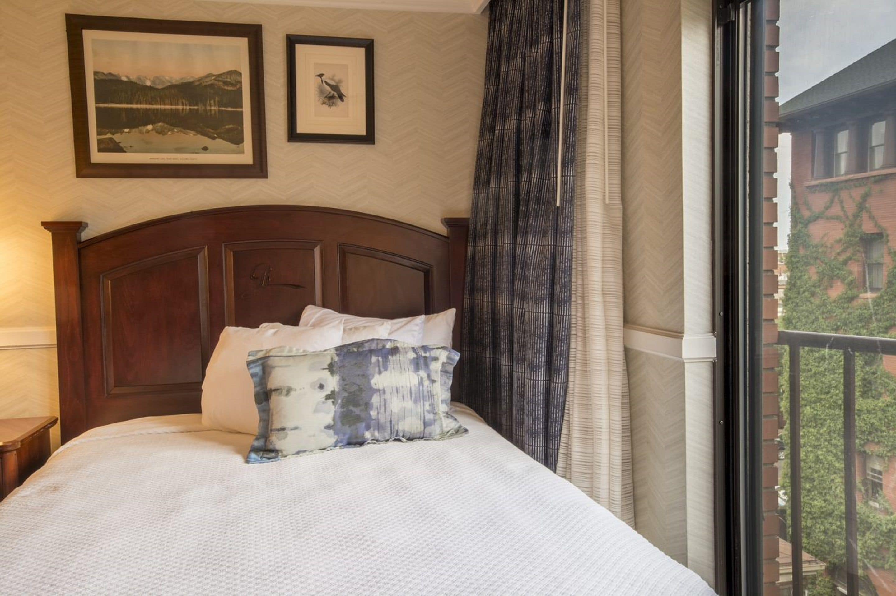 A neatly made bed with a patterned pillow, a wooden headboard, and two framed pictures on the wall.