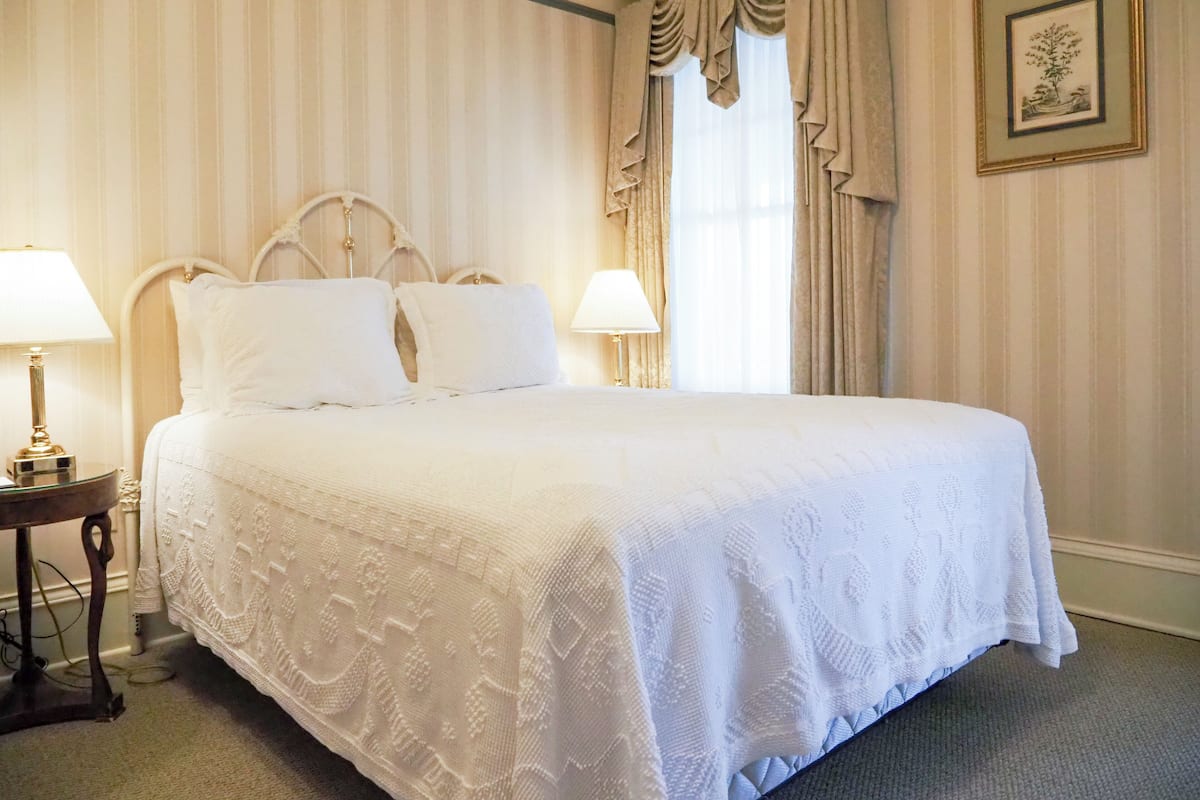 A neatly made bed with a white bedspread, two bedside lamps, and a framed picture on the wall.