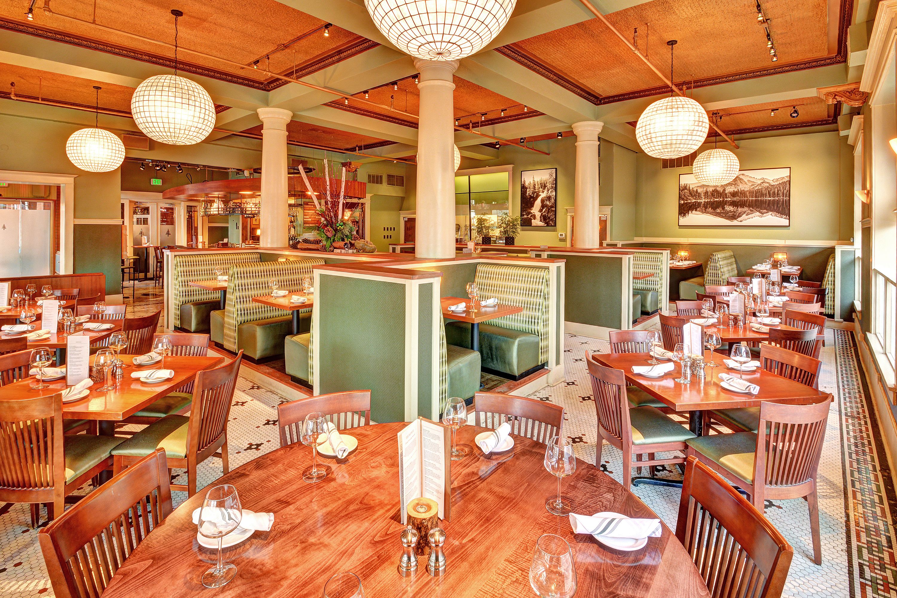 A restaurant with wooden tables, green booths, and hanging spherical light fixtures.