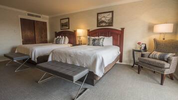 A hotel room with two beds, a bench, a chair, and a nightstand with a lamp.