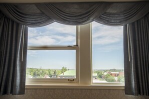 A window with dark curtains, a view of a green landscape, and a clear sky.