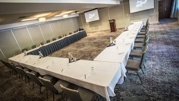 Un salón de conferencias con una mesa larga, sillas, un atril y una pantalla.