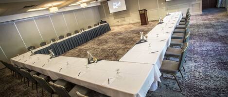 A conference room with a long table, chairs, a podium, and a screen.