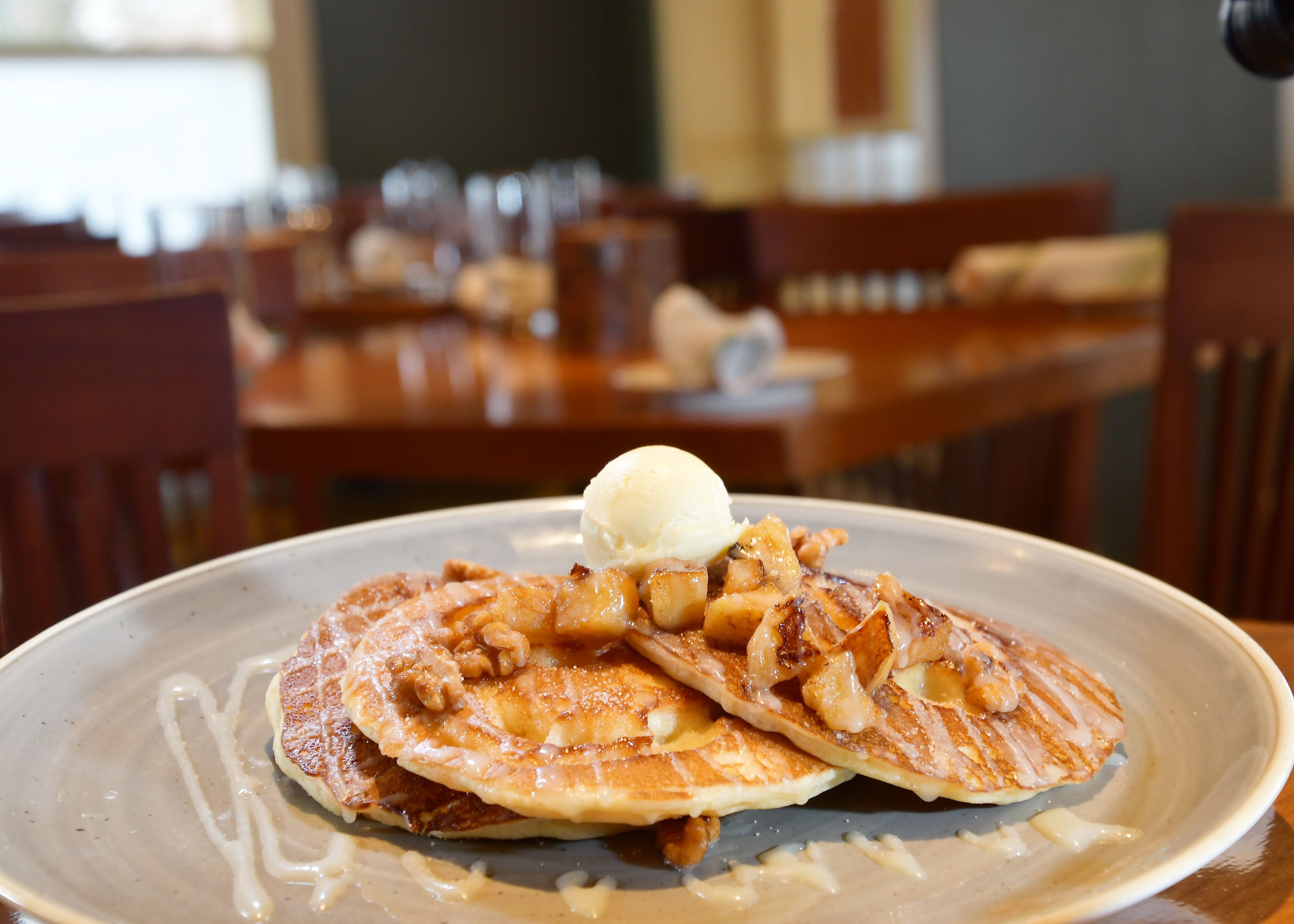 A plate of pancakes with apple slices and a scoop of ice cream on a ceramic plate.