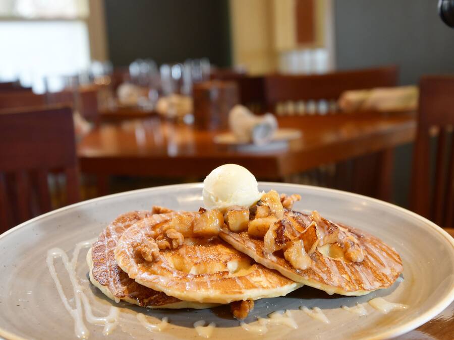 A plate of pancakes with apple slices and a scoop of ice cream on a ceramic plate.
