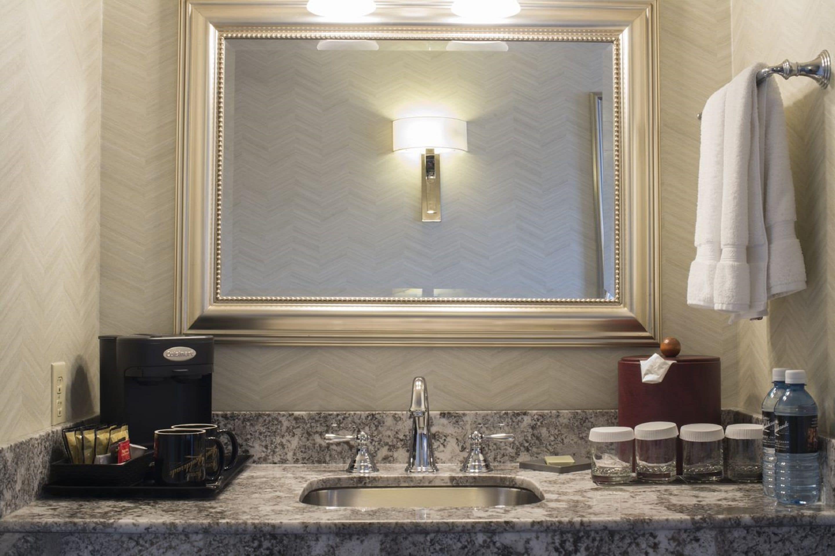 A bathroom with a large mirror, a sink, a coffee maker, and toiletries.