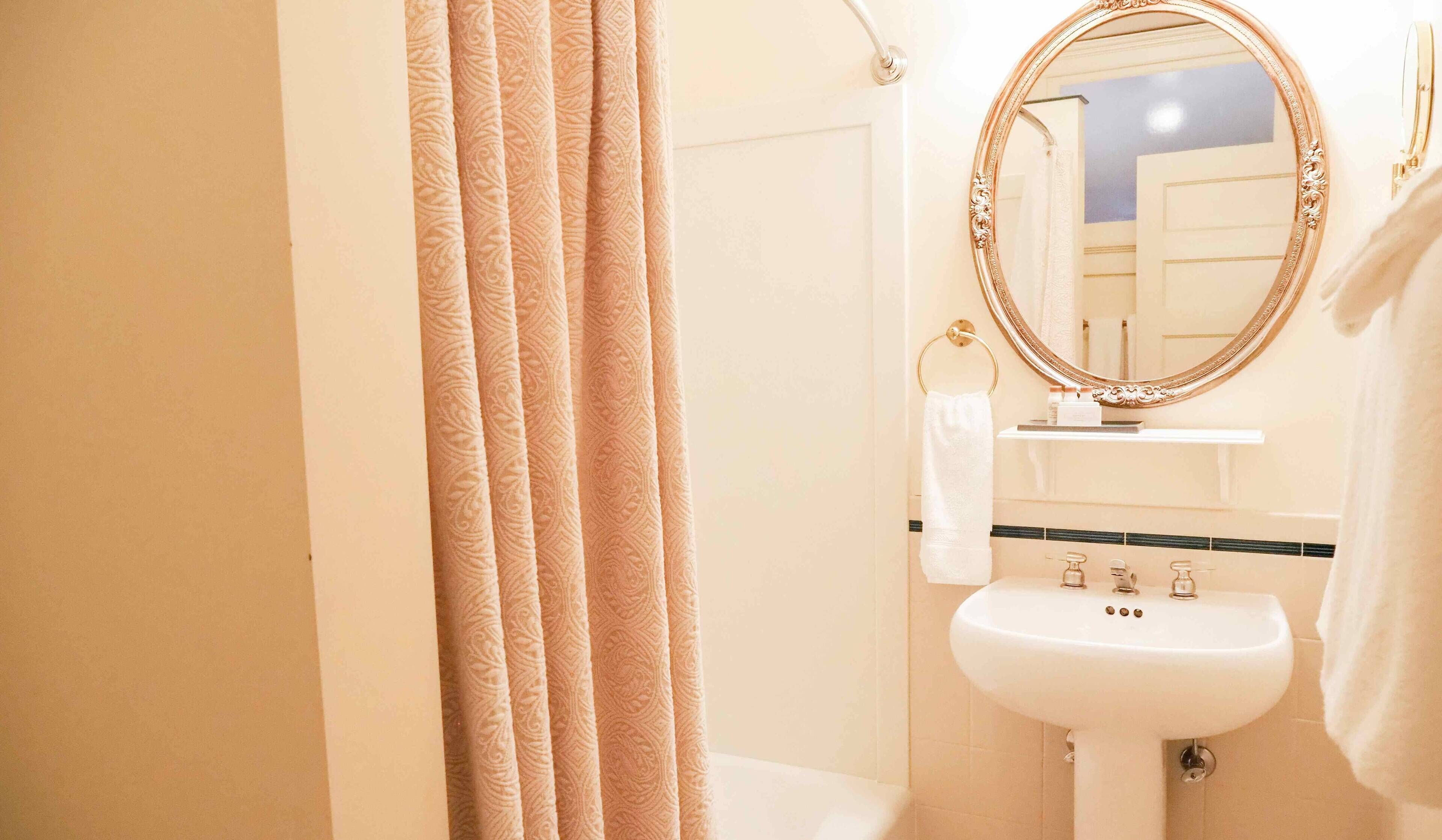 A bathroom with a white sink, a gold-framed mirror, and beige curtains.