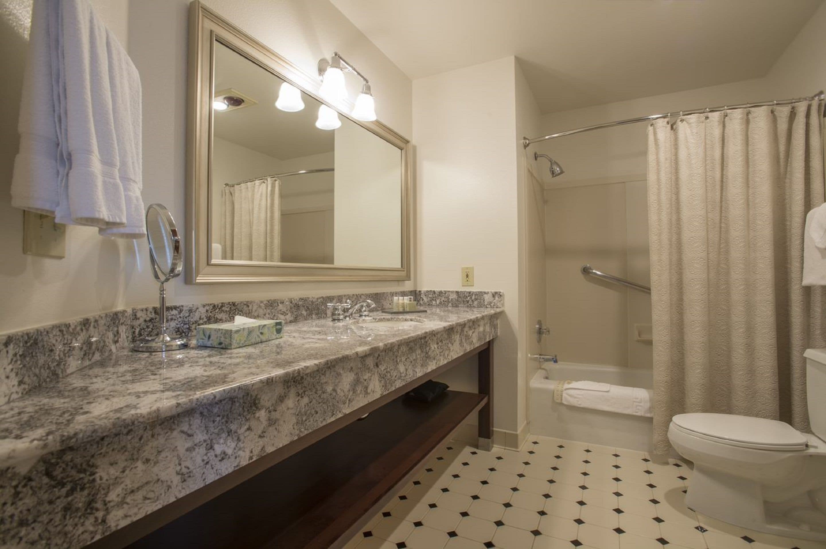 A bathroom with a marble countertop, a large mirror, a shower with a glass door, and a toilet.