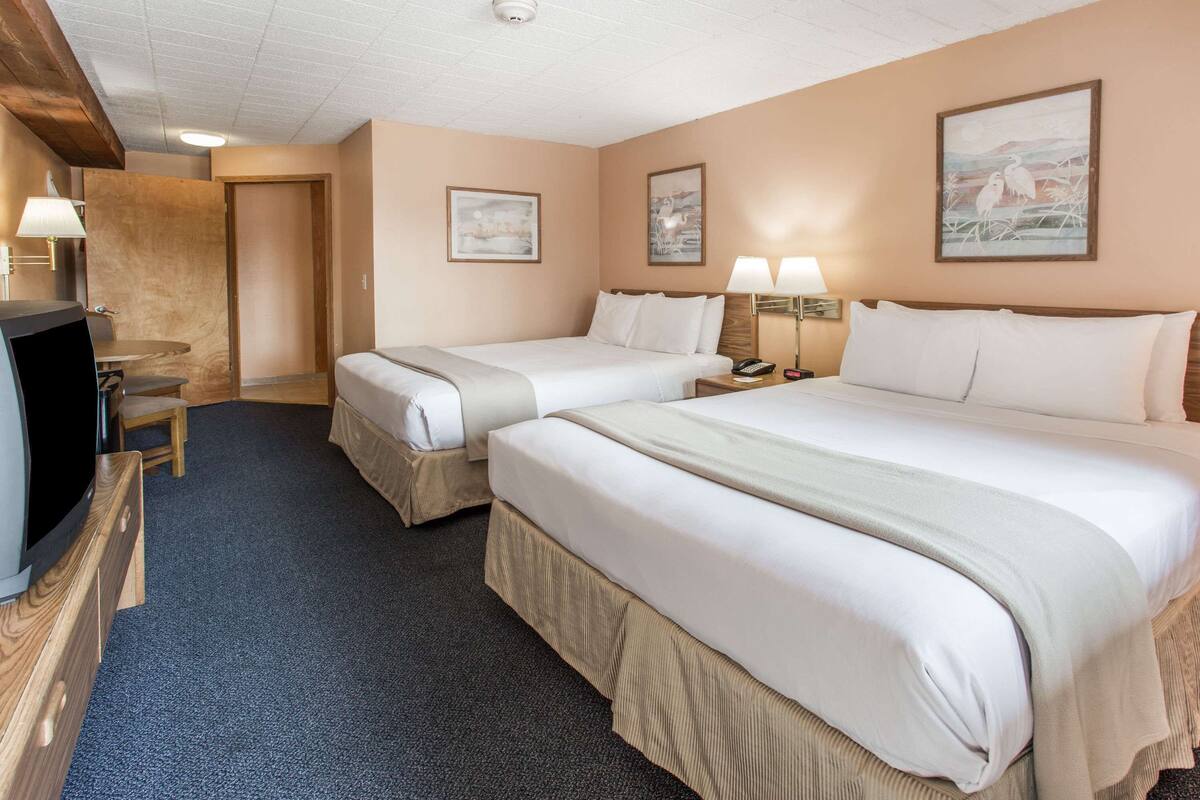 A hotel room with two beds, a desk, and a television.
