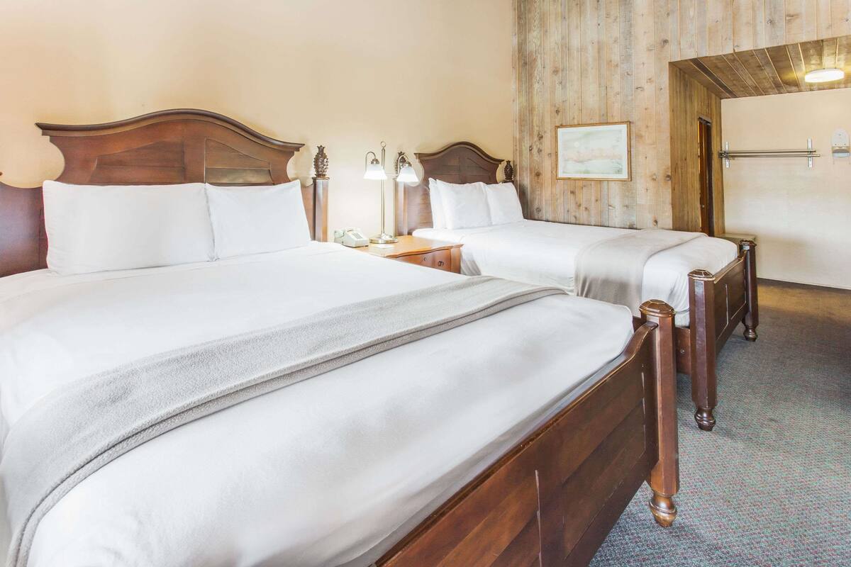 A hotel room with two wooden beds, a nightstand with a lamp, and a wooden wall panel.