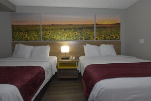 Une chambre d’hôtel avec deux lits, une table de chevet avec une lampe et une grande fresque murale représentant un champ de tournesols.