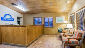 A reception area with a wooden reception desk, a Days Inn logo, a seating area with striped chairs, and a city view through the windows. - Days Inn by Wyndham West Allis/Milwaukee (Milwaukee)