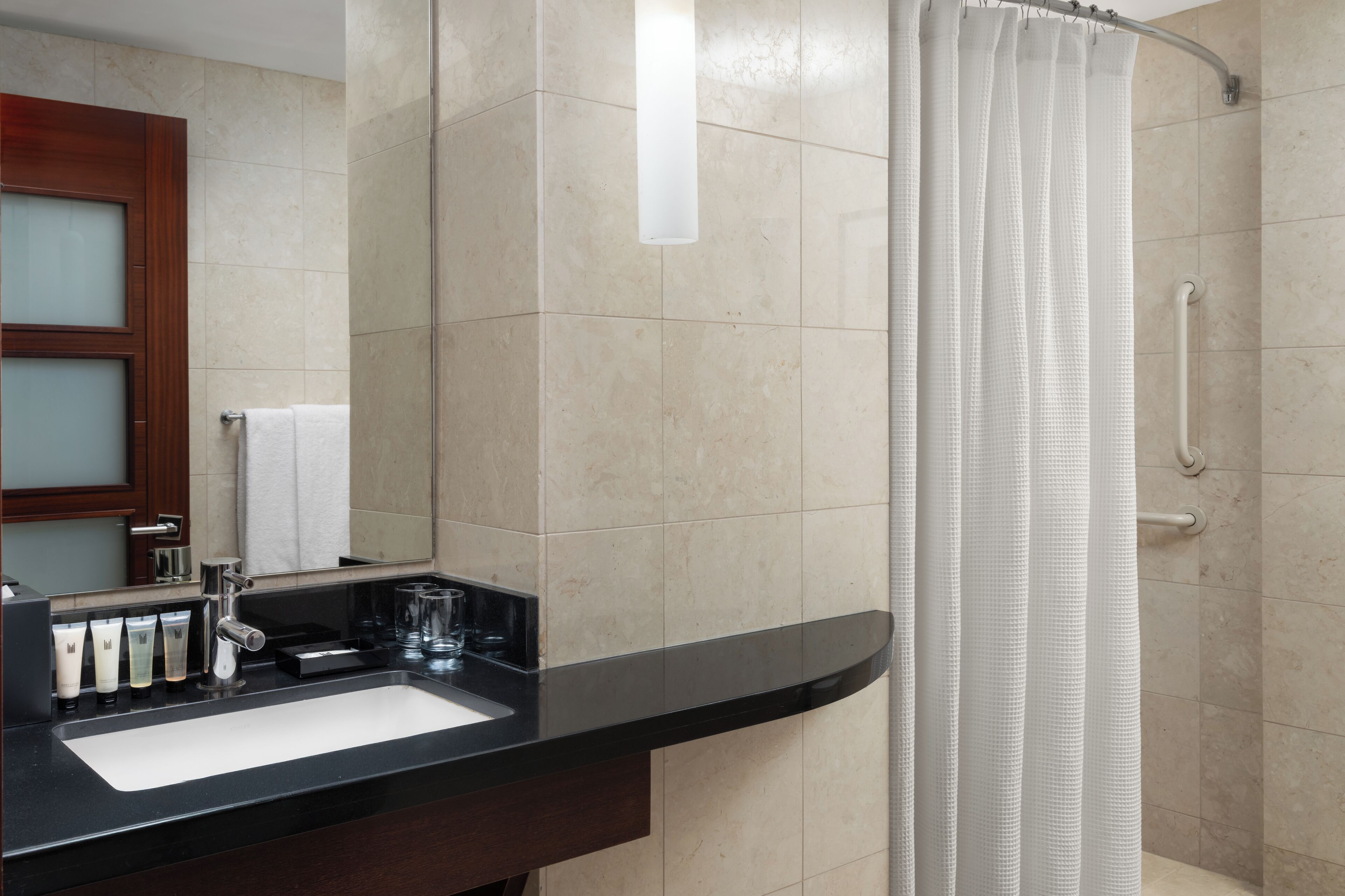 Un baño con encimera negra, lavabo y ducha con cortina blanca.