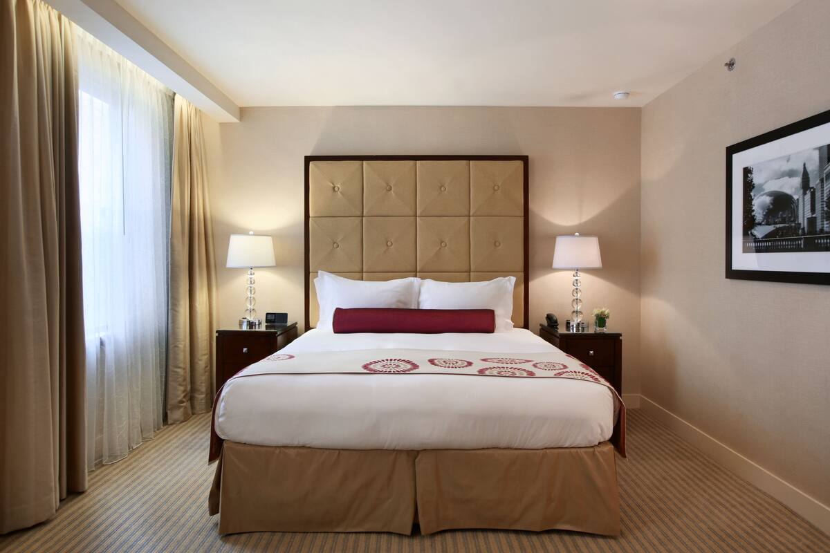 A hotel room with a large bed, two bedside tables, a headboard, and a framed picture on the wall.