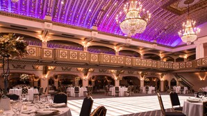Um salão de banquetes com teto ricamente decorado, lustres e mesas montadas para um evento formal.