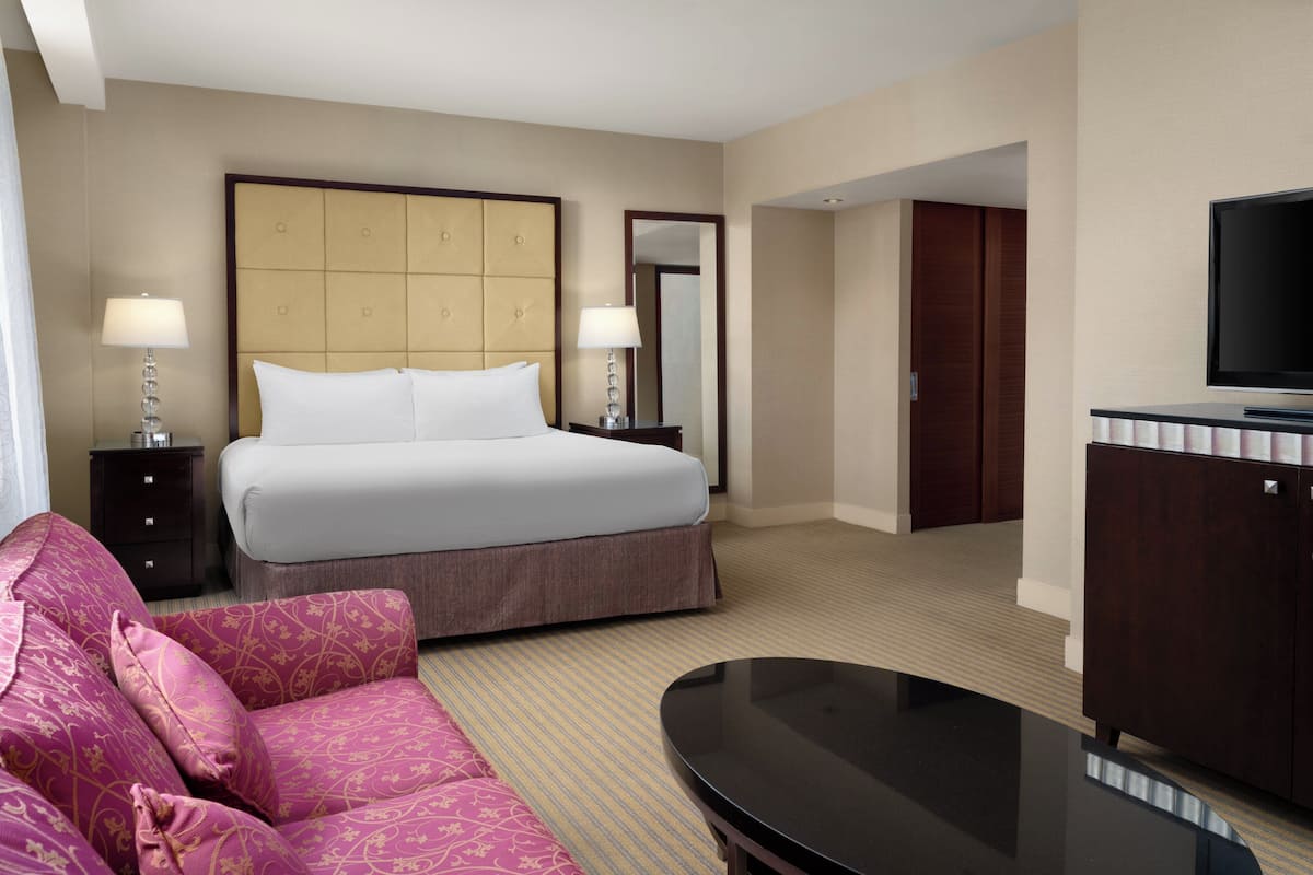 A hotel room with a bed, two bedside lamps, a television, a sofa, and a mirror.