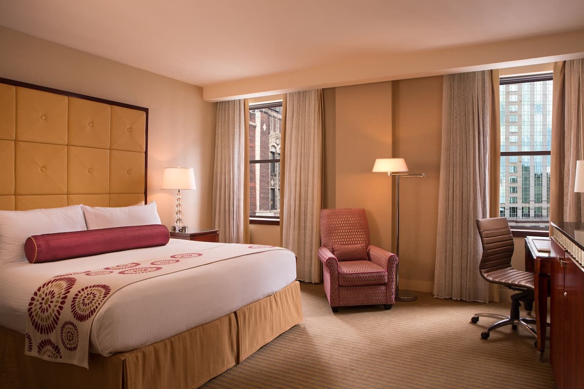 A hotel room with a large bed, a desk, a chair, and a window with curtains.