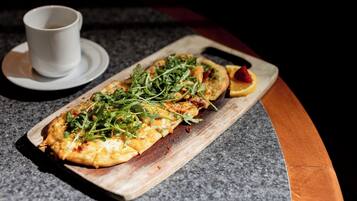 A long, narrow dish with greens and a slice of orange on a wooden board, accompanied by a white cup on a saucer.