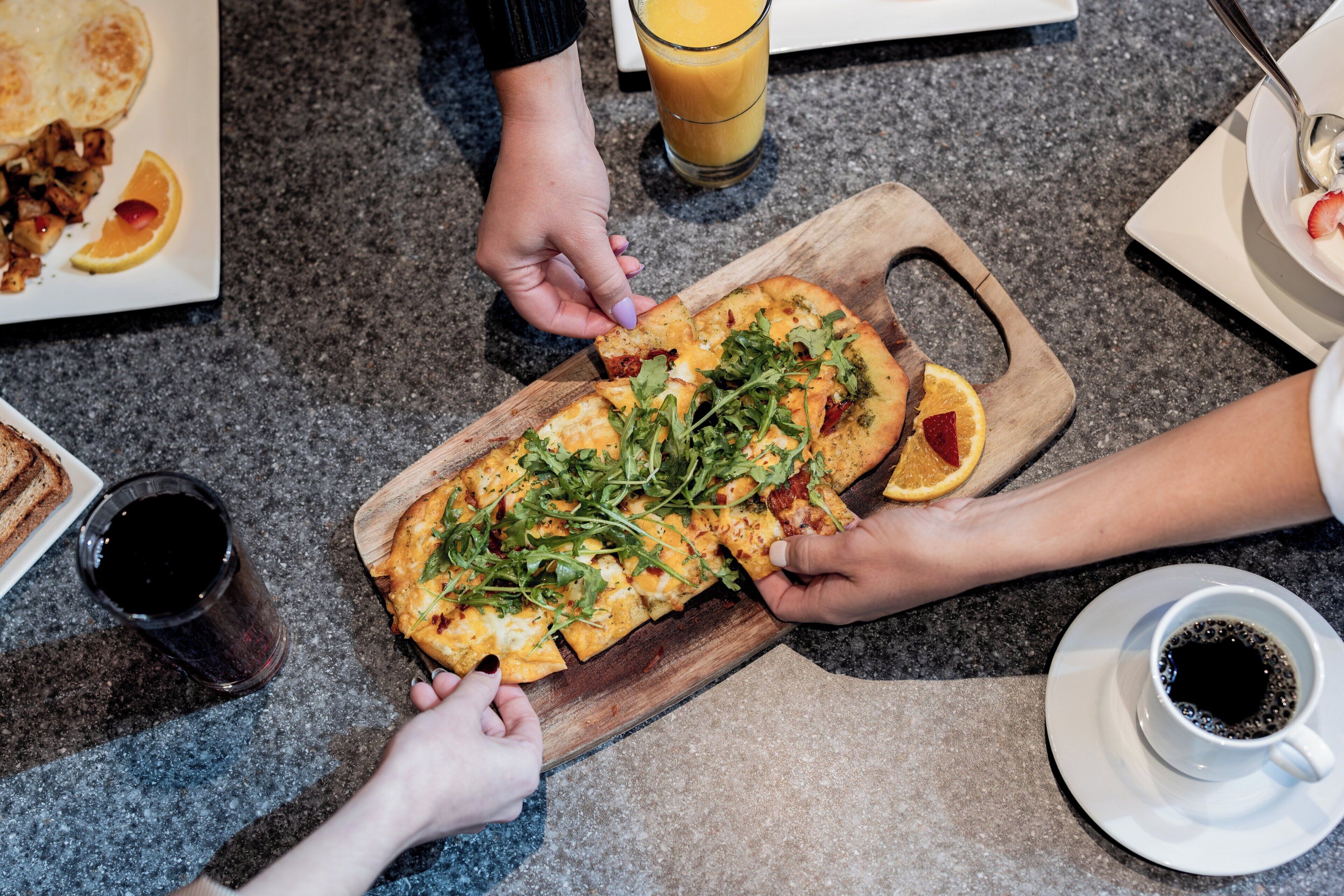 Un pasto con pizza su un tagliere di legno, un bicchiere di succo d'arancia e una tazza di caffè su un tavolo.
