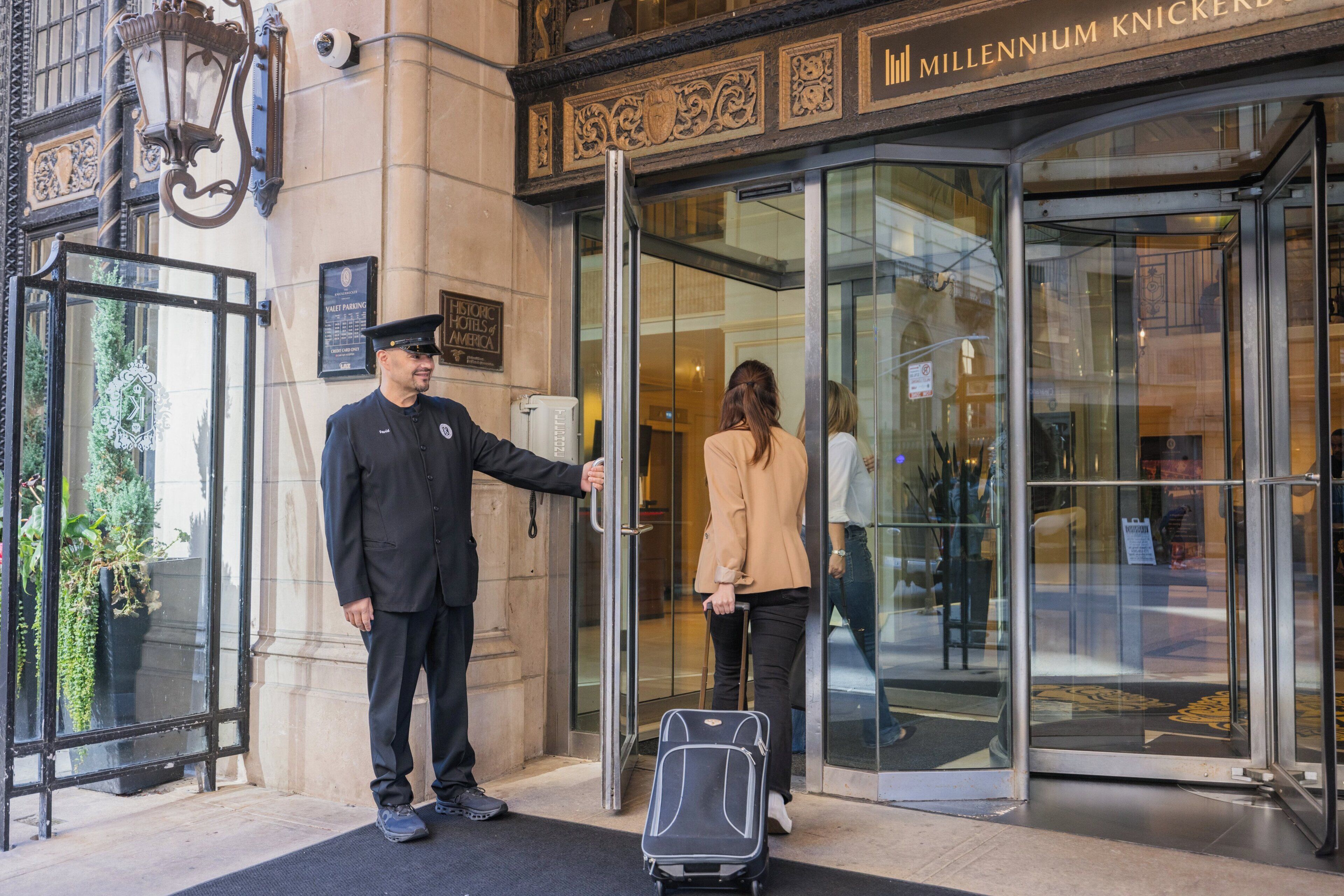 A hotel entrance with a glass door, a security guard, and a person with luggage.