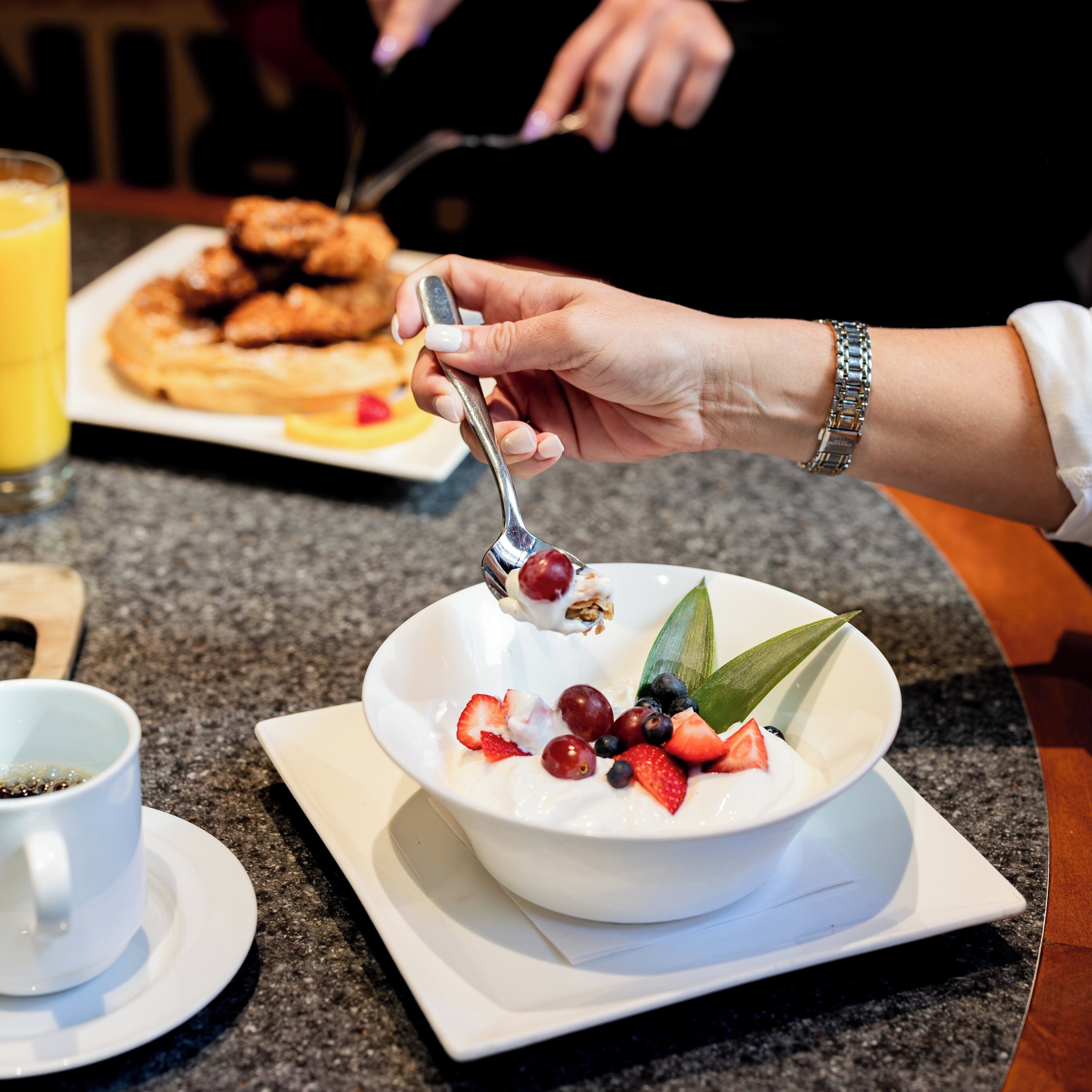 Une table mise pour le petit-déjeuner, avec un bol de yaourt garni de fruits et une cuillère.