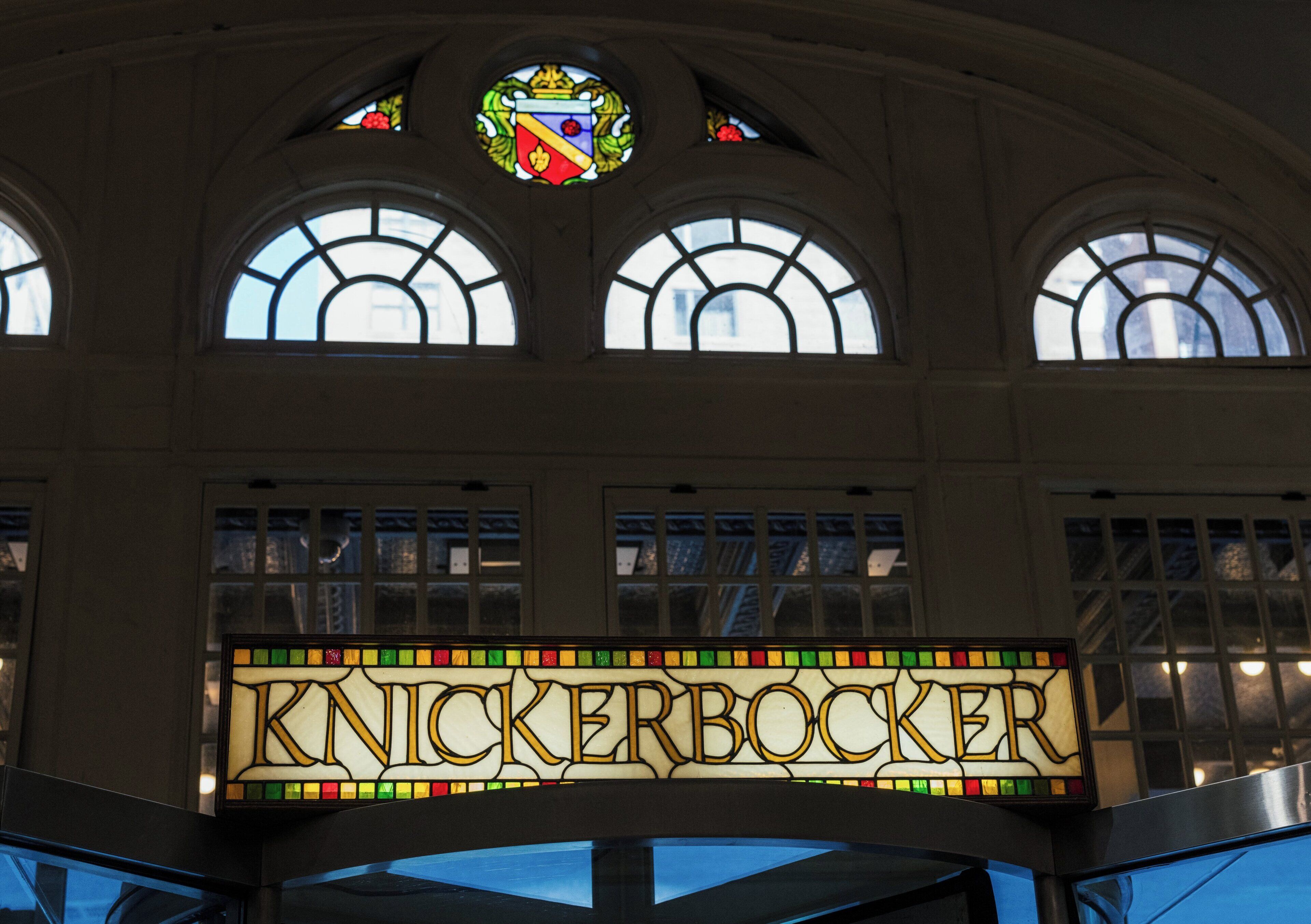 Un cartel de vitral con el nombre 'KNICKERBOCKER' en un edificio con ventanas arqueadas y un vitral en la parte superior.