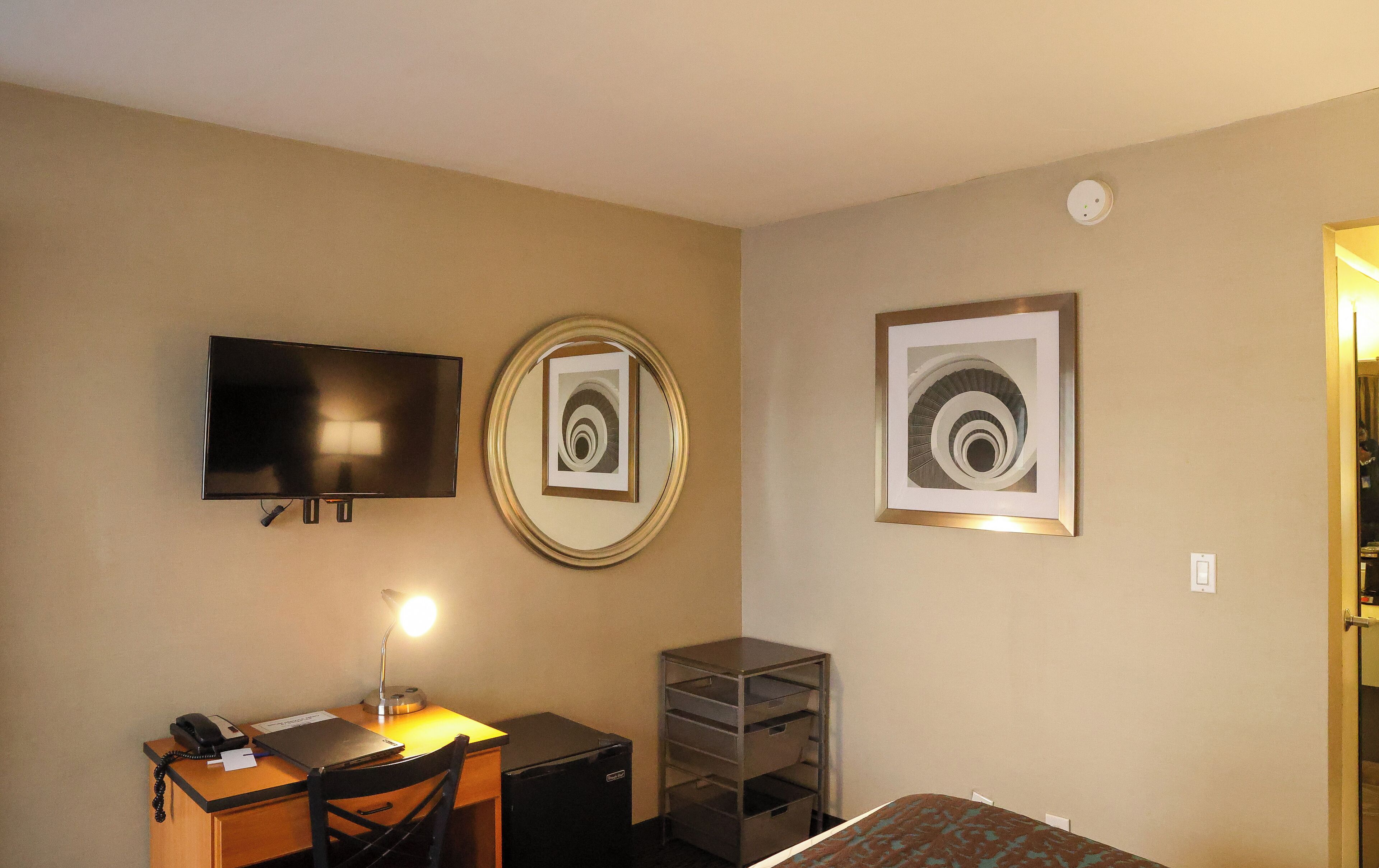 A hotel room with a desk, chair, TV, lamp, and artwork on the walls.