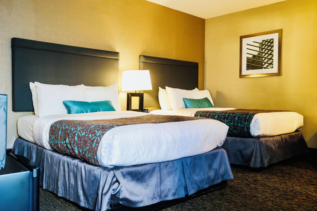 A hotel room with two beds, a nightstand with a lamp, and a framed picture on the wall.