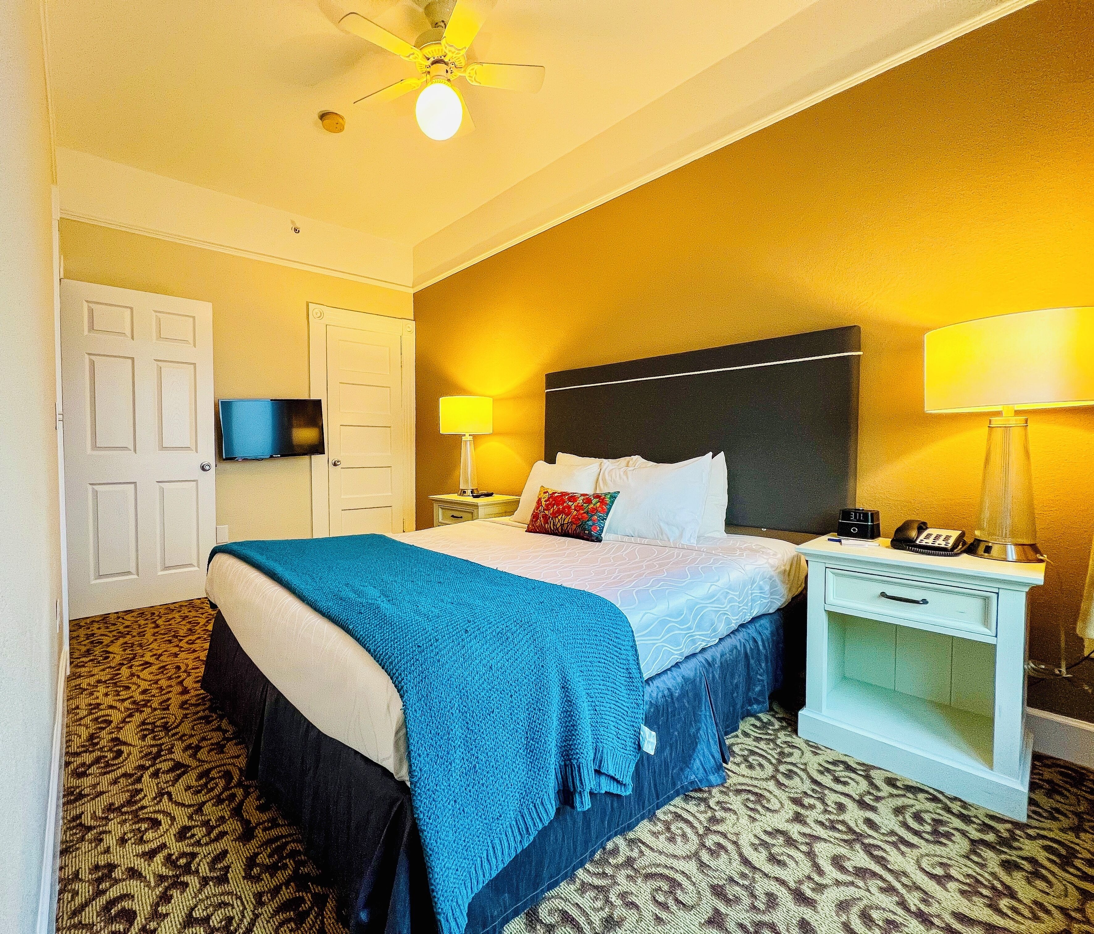 A hotel room with a bed, bedside tables, a TV, and a ceiling fan.