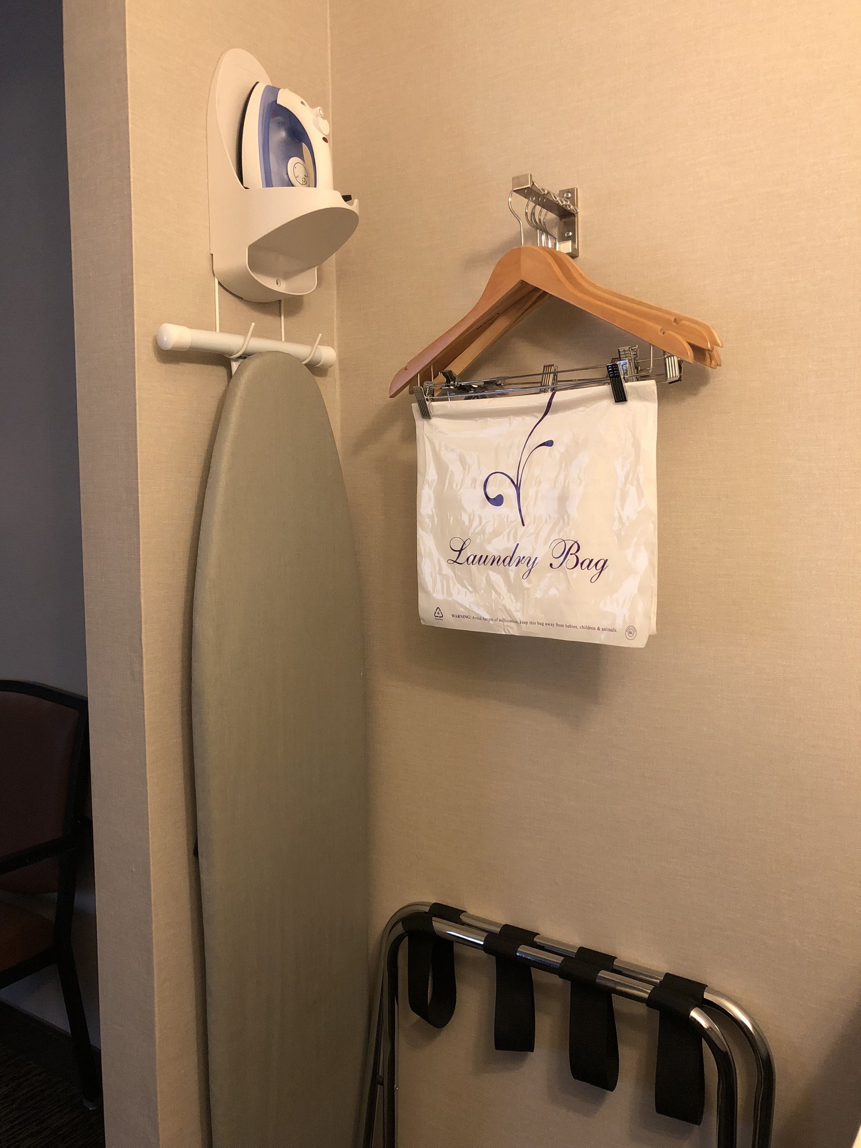 Une salle de bain équipée d’une planche à repasser, d’un fer à repasser et d’un sac à linge suspendu.