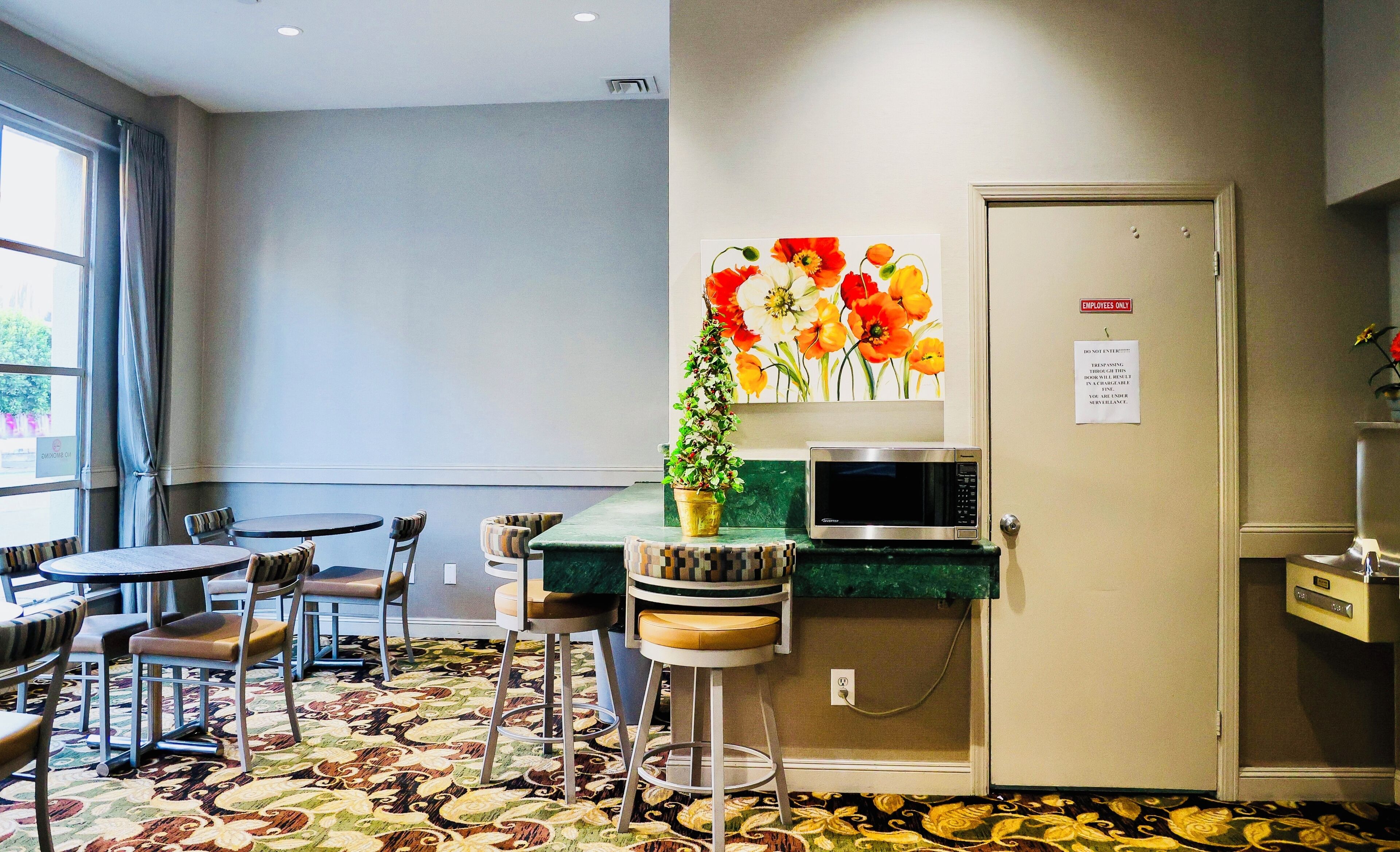 A hotel room with a dining area, a microwave, a potted plant, and a door with a sign indicating it is for employees only.