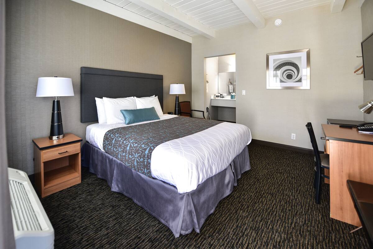 A hotel room with a large bed, two bedside tables with lamps, a desk, and a chair.