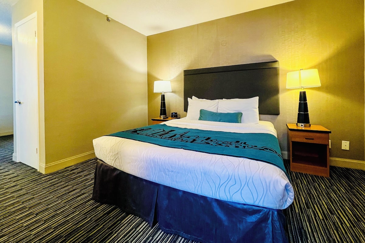 A hotel room with a large bed, two bedside tables, and two lamps.