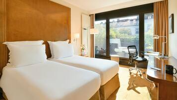 Habitación de hotel con dos camas, un escritorio con silla, una lámpara y vistas al exterior.