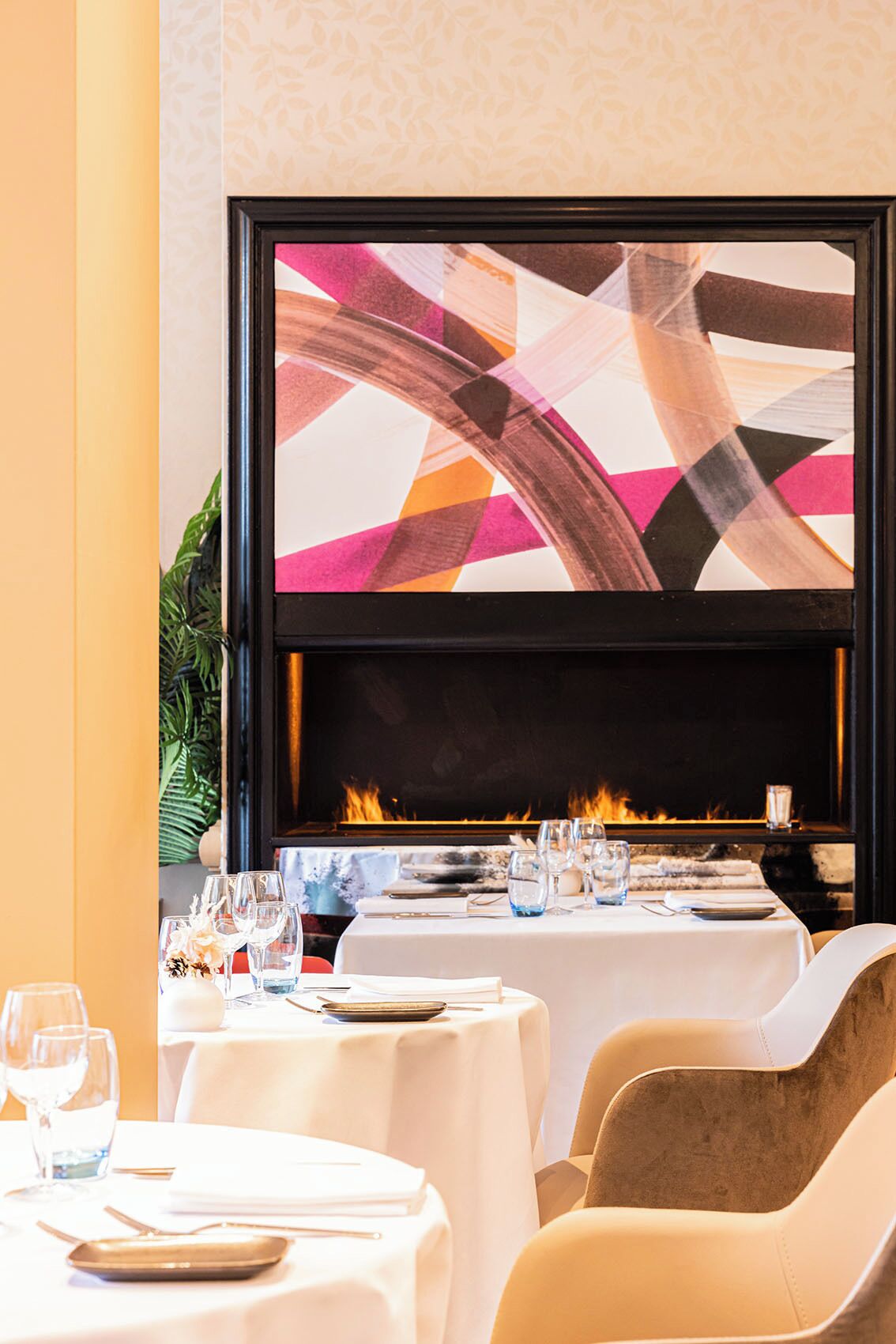 A restaurant with a fireplace, tables set for dining, and a large abstract painting above the fireplace.