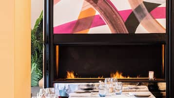A restaurant with a fireplace, tables set for dining, and a large abstract painting above the fireplace.
